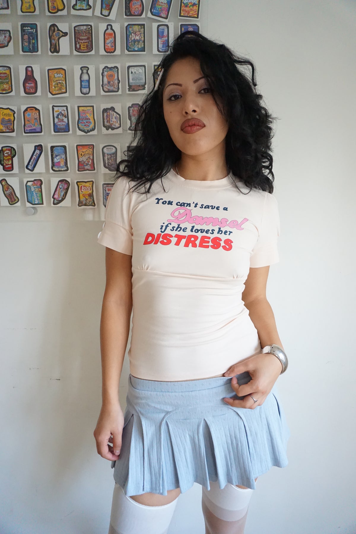 girl wearing peach pink t shirt with buttons on the sleeve and a graphic that says "you can’t save a damsel if she loves her distress"
