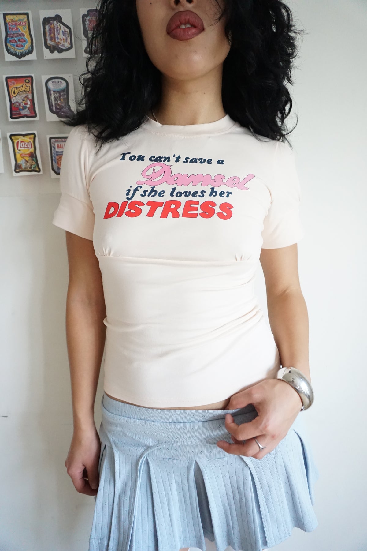 peach pink t shirt with buttons on the sleeve and a graphic that says "you can’t save a damsel if she loves her distress"
