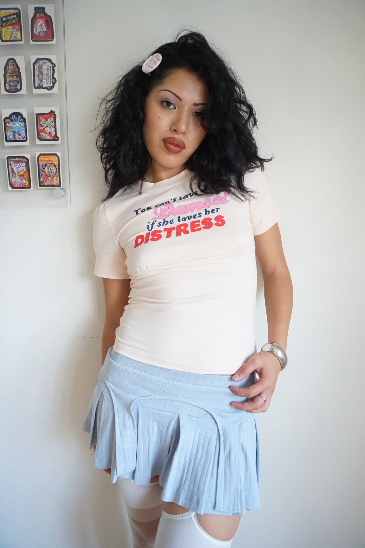 girl wearing peach pink t shirt with buttons on the sleeve and a graphic that says "you can’t save a damsel if she loves her distress"