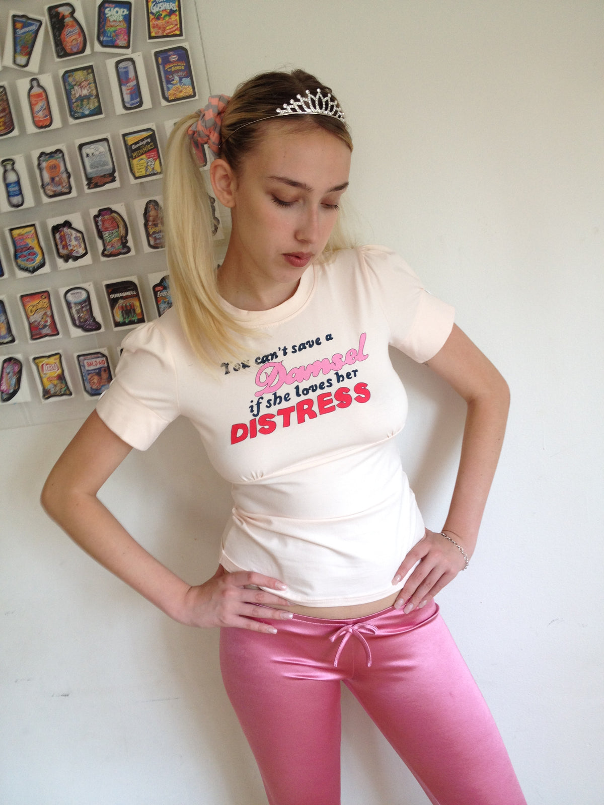 girl wearing a peach t shirt with buttons on the sleeve and a graphic that says "you can’t save a damsel if she loves her distress"