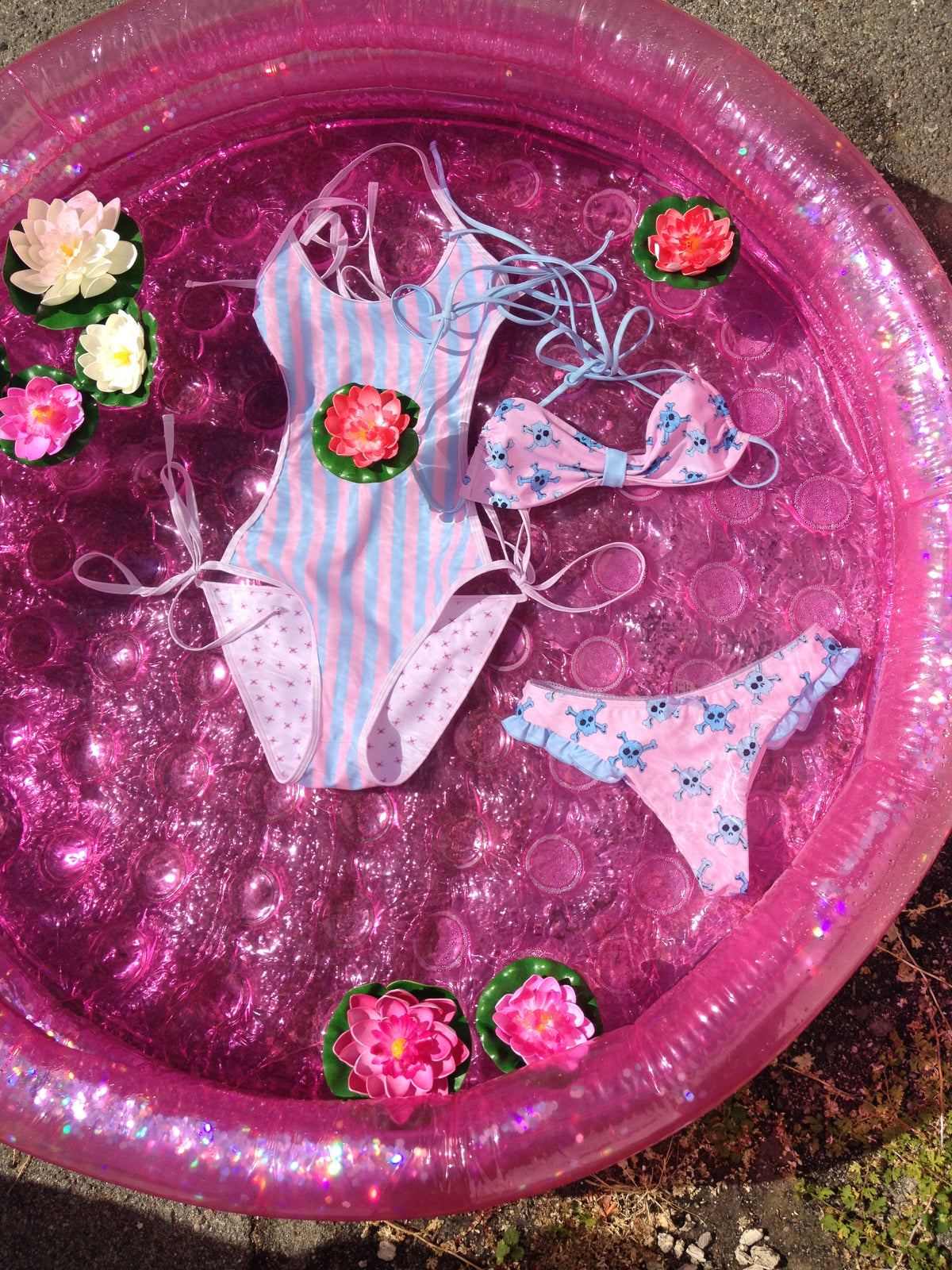 two bathing suits floating in a pink pool with floating lotus flowers 