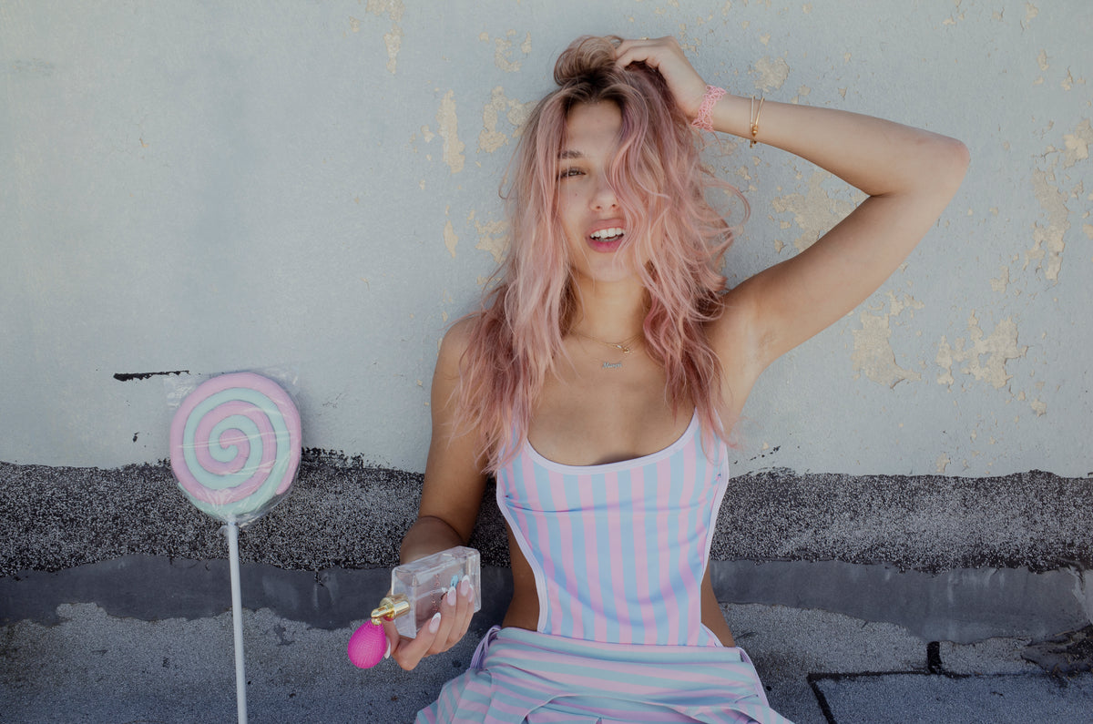 Girl wearing a pink and blue stripe one piece swimsuit with cutouts on side with lollipop
